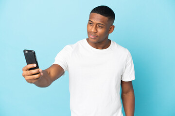 Young latin man isolated on blue background making a selfie with mobile phone