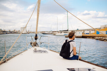 Guy traveler with a backpack sits on a sailing yacht and enjoys the views. A man on a yacht in the...