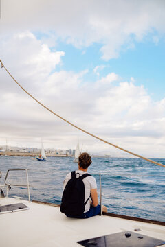 Guy traveler with a backpack sits on a sailing yacht and enjoys the views. A man on a yacht in the ocean, summer day.