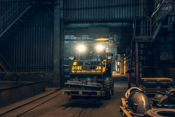 Fototapeta premium Small yellow loading tractor or mower at work in metallurgical factory workshop.