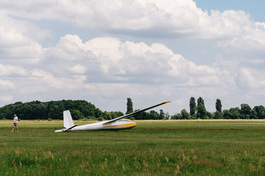 Man preparing and checking glider parked in the field, aerodrome for training, small plane ready to fly. Small aviation extreme sport leisure activity. 