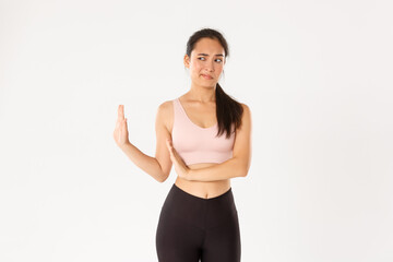 Fototapeta na wymiar Sport, wellbeing and active lifestyle concept. Displeased and unamused asian fitness girl showing block with hand and looking left disgusted, express aversion and reject something bad