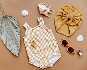 Cute retro swimsuit for baby girl with seashells and beach accessories on brown background. Summer...