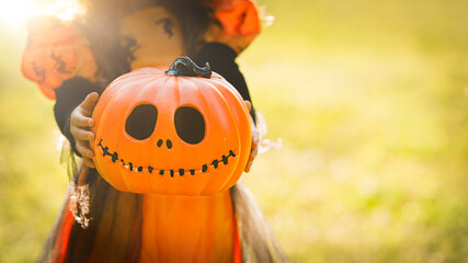 Pumpkin head Jack-o'-lantern in the hands of a girl in a witch costume on the street with a copy space, background for Halloween