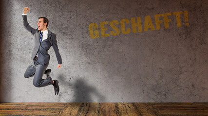 jumping and happy businessman and German message for DONE in front of a concrete wall