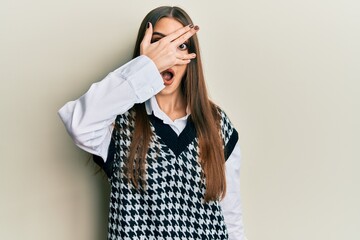 Beautiful brunette young woman wearing casual clothes peeking in shock covering face and eyes with hand, looking through fingers afraid