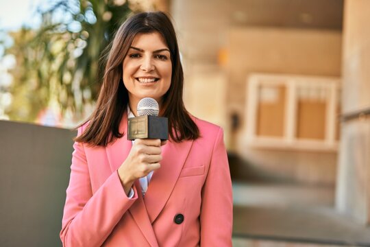 Middle age reporter woman holding microphone doing television speech outdoors
