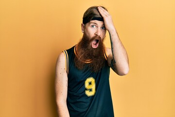 Redhead man with long beard wearing basketball uniform surprised with hand on head for mistake,...