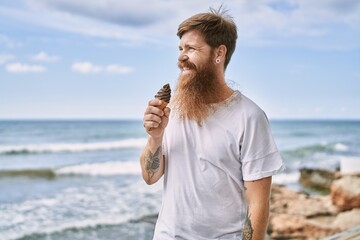 Young redhead man smiling happy eating ice cream at the beach.
