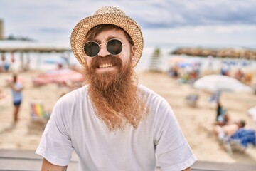 Young redhead tourist man smiling happy sitting on the bench at the beach.