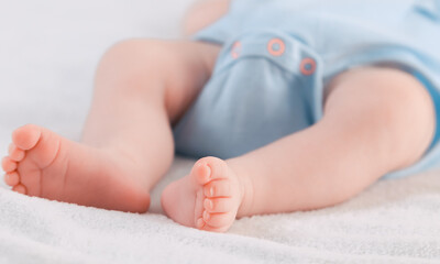 Legs with toes of a sleeping  newborn.
Legs with toes of a sleeping Caucasian newborn in a blue bodysuit lying on the right diagonally in bed on a white fleece blanket, very close-up side view. 