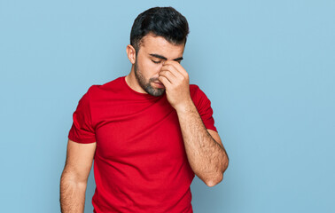 Hispanic man with beard wearing casual red t shirt tired rubbing nose and eyes feeling fatigue and...