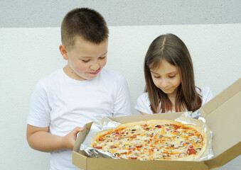 Cute girl and a boy eating a big delicious pizza outdoors
