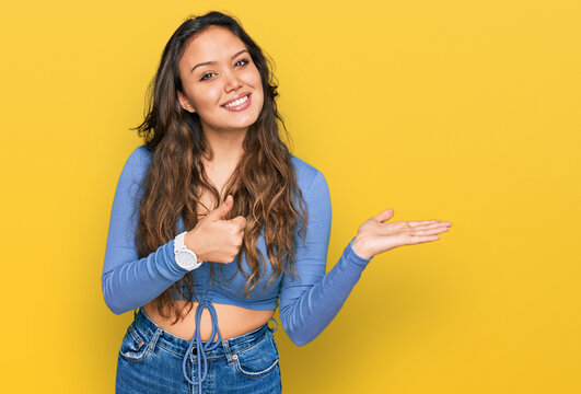 Young hispanic girl wearing casual clothes showing palm hand and doing ok gesture with thumbs up, smiling happy and cheerful