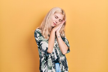 Beautiful caucasian woman with blond hair wearing tropical shirt sleeping tired dreaming and posing with hands together while smiling with closed eyes.