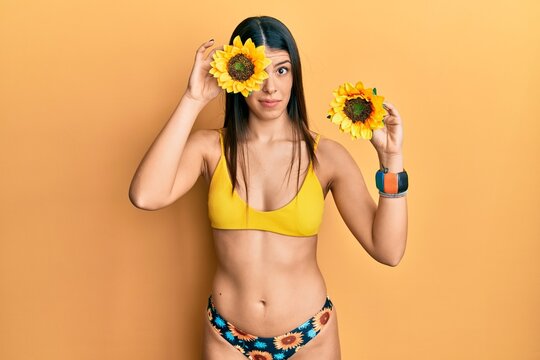 Young hispanic woman wearing bikini holding sunflowers skeptic and nervous, frowning upset because of problem. negative person.