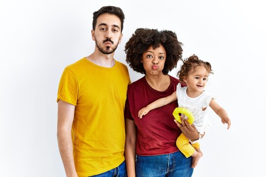 Interracial young family of black mother and hispanic father with daughter puffing cheeks with funny face. mouth inflated with air, crazy expression.