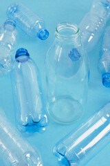 one glass bottle among several plastic bottles on a blue background