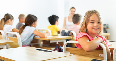 Young girl sitting at desk in class room. She have turned around and looking in camera.