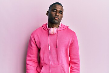 Young african american man wearing gym clothes and using headphones relaxed with serious expression on face. simple and natural looking at the camera.