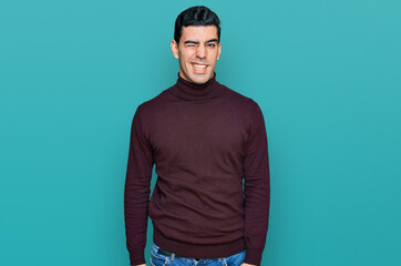Handsome hispanic man wearing casual turtleneck sweater winking looking at the camera with sexy...
