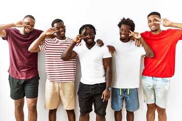 Young african group of friends standing together over isolated background doing peace symbol with fingers over face, smiling cheerful showing victory