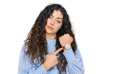 Young hispanic girl wearing casual clothes in hurry pointing to watch time, impatience, looking at the camera with relaxed expression