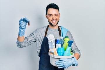 Young hispanic man holding cleaning products and cockroach winking looking at the camera with sexy...