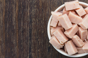 Turkey breast cubes in a white pot isolated on a wooden cutting board. Selective focus. Top view.