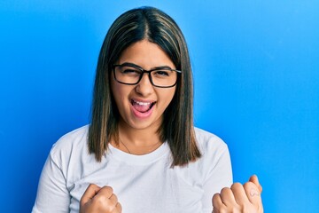 Young latin woman wearing casual clothes and glasses celebrating surprised and amazed for success...