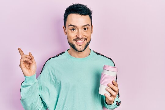 Young hispanic man drinking a cup of coffee smiling happy pointing with hand and finger to the side
