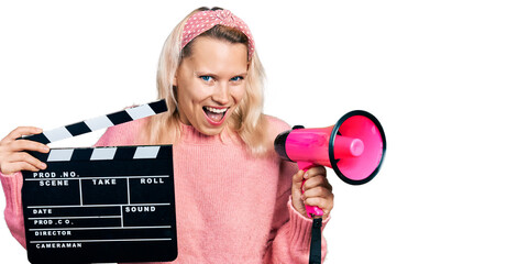 Young caucasian woman holding video film clapboard and megaphone smiling and laughing hard out loud...