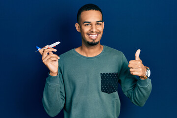 Young african american man holding airplane toy smiling happy and positive, thumb up doing excellent and approval sign