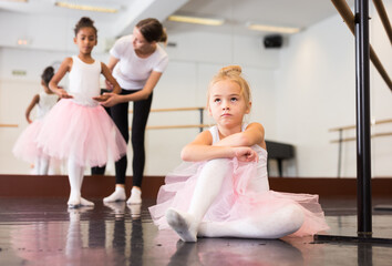 Little upset girl in pink tutu sitting on floor in ballet class