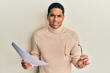 Young handsome hispanic man holding blank paper and glasses clueless and confused expression. doubt...