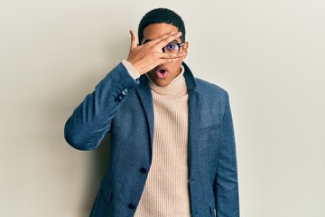 Young handsome hispanic man wearing elegant clothes and glasses peeking in shock covering face and eyes with hand, looking through fingers with embarrassed expression.