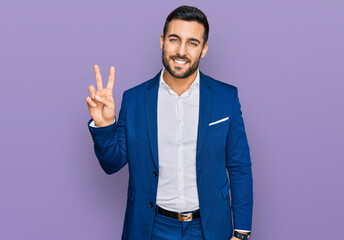 Young hispanic man wearing business jacket smiling looking to the camera showing fingers doing victory sign. number two.