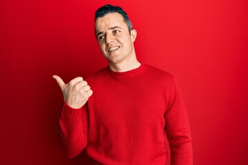 Handsome young man wearing casual winter sweater pointing thumb up to the side smiling happy with open mouth