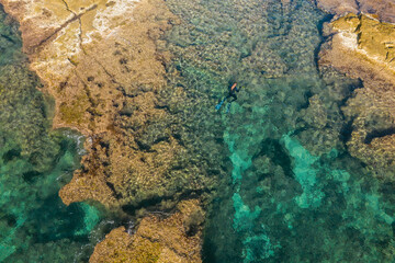 Aerial drone bird's eye view of swimming spearfishing diver in rocky seascape located in Costa Blanca, Torrevieja, Spain