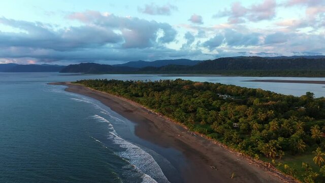 Drone flight along Zancudo peninsula with palm trees and mountains during sunset Costa Rica 