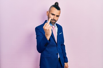 Young hispanic man wearing business suit and tie showing middle finger, impolite and rude fuck off...