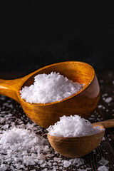 Healthy sea salt in crystals on wooden spoon closeup. Close up Low key composition on dark rustic wooden background. Selective focus.