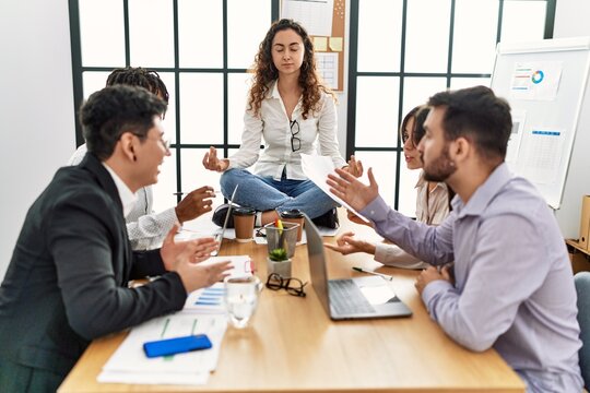 Businesswoman enjoys meditating during meeting. Sitting on desk near arguing partners at the office.