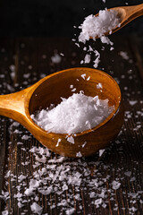 Spilled sea salt in crystals on wooden spoons closeup. Close up Low key composition on dark rustic wooden background. Selective focus.