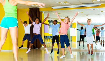 happy sportive children with female teacher training in modern dance hall, jumping together