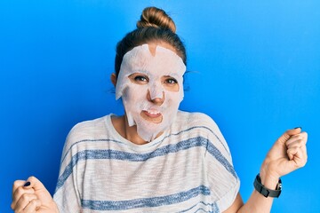 Young blonde woman wearing beauty face mask screaming proud, celebrating victory and success very excited with raised arm