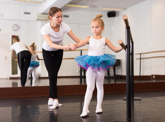 Female classical dance trainer teaching little ballerina in ballet class.