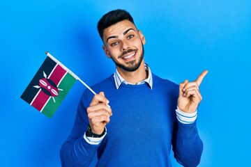 Young hispanic man with beard holding kenya flag smiling happy pointing with hand and finger to the side