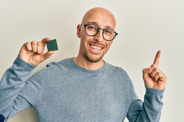 Bald man with beard holding cpu computer processor smiling happy pointing with hand and finger to...