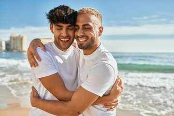 Young gay couple smiling happy hugging at the beach.